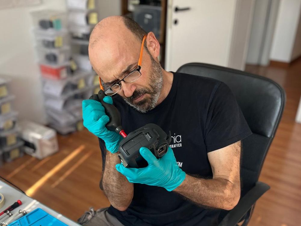 Francesco Borioni blower-cleaning a camera body at the European Camera Repair bench in Ancona